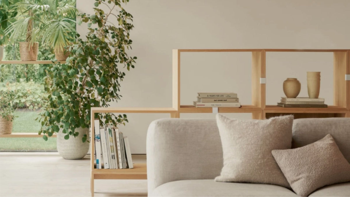 Roligt opholdsrum med sofa, puder, planter og bogreol, hvor bløde materialer og indretning er med til at dæmpe rumklang i hjemmet