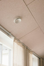 Arku rektangulært akustikpanel i lys sand. I moderne bolig monteret i loft til kip tilpasset til ventilationskanal tæt på vinduer med gardiner.